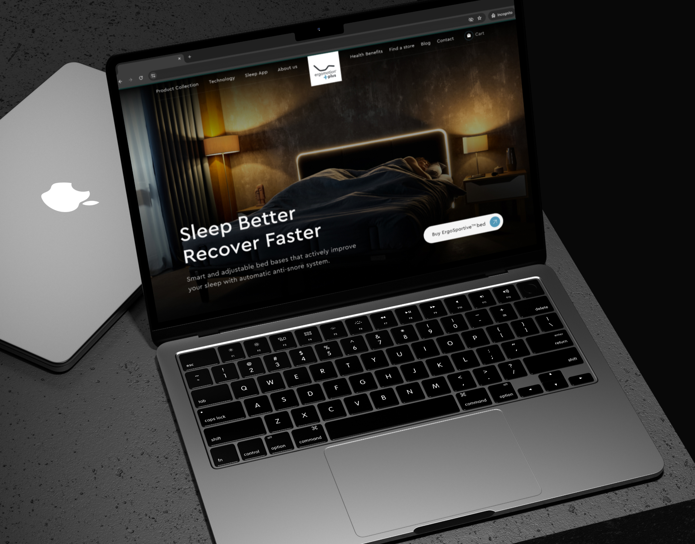Ergomotion Plus Sleep Better Recover Faster homepage on a MacBook resting on dark concrete beside a closed laptop
