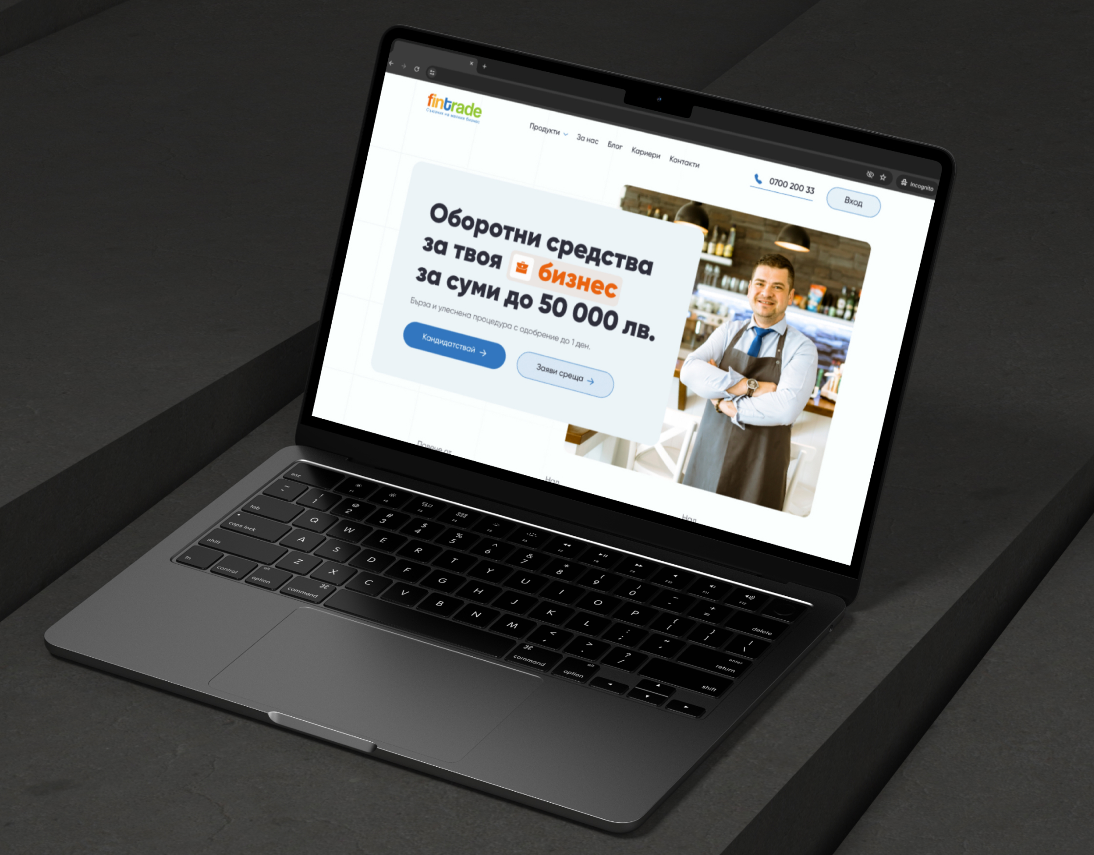 Fintrade homepage on an angled laptop mockup on a dark grey surface, showing the working capital hero and photo