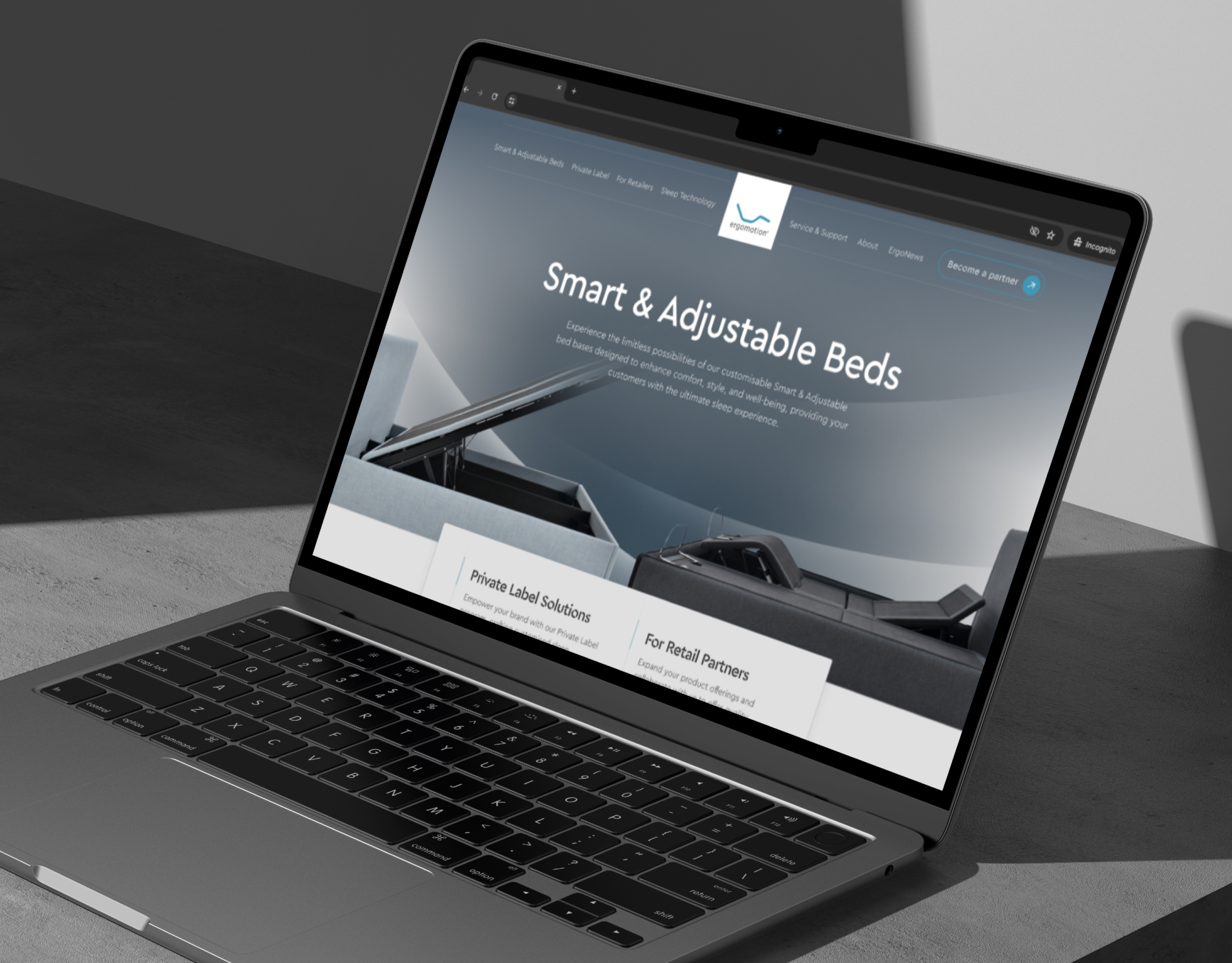 Ergomotion's Smart and Adjustable Beds homepage on a laptop screen, angled on a dark concrete surface