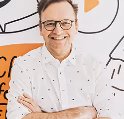 Portrait photo of Klaus Schwope, smiling and looking into the camera with his arms crossed.
