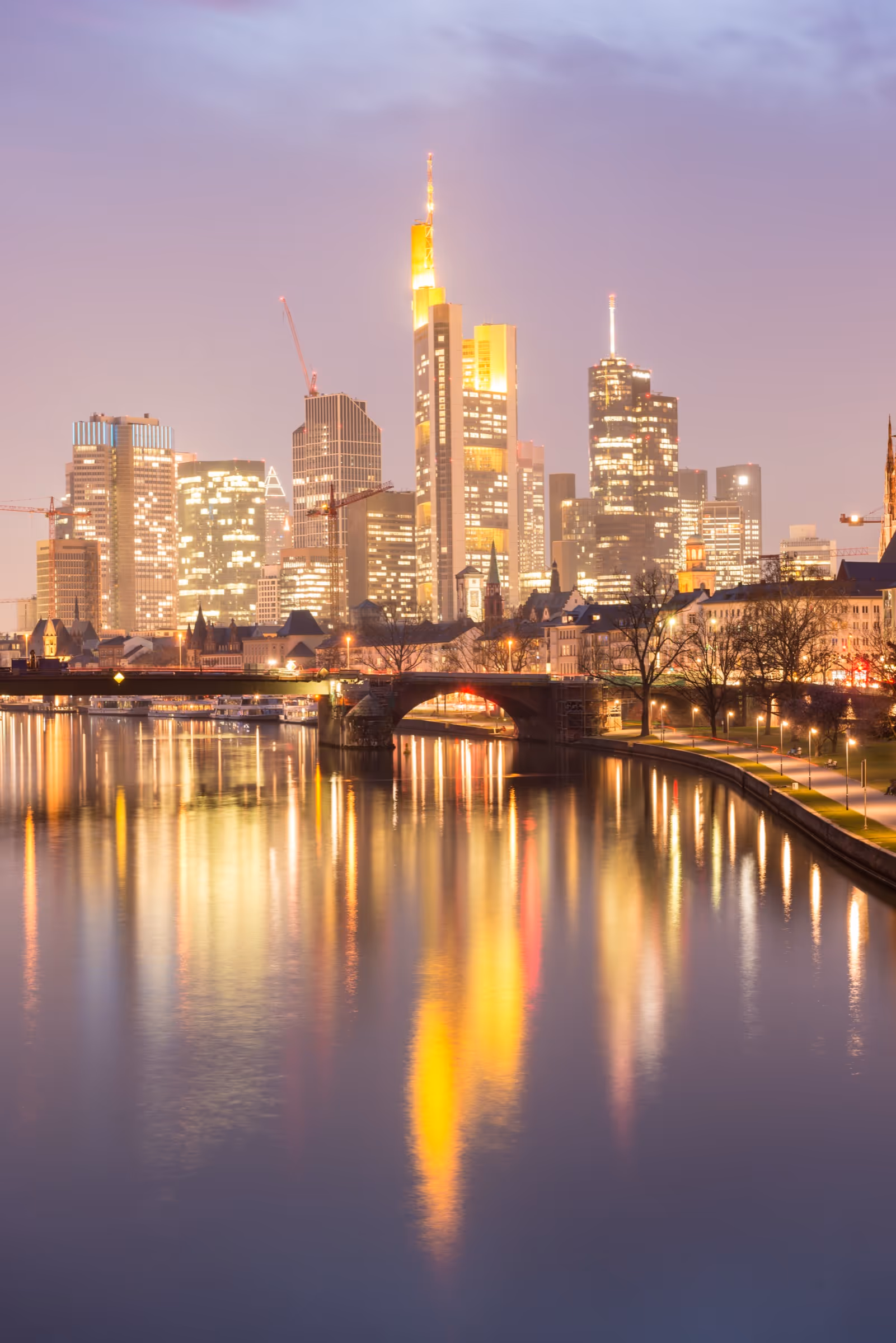 Frankfurts beleuchtete Skyline mit reflektierenden Lichtern auf dem Fluss am Abend.