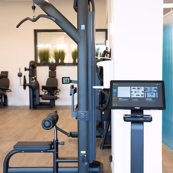 Blick in den großen hellen Trainingsbereich mit Fokus auf den Latissimus-Zug und die Technogym Check-In-Station.