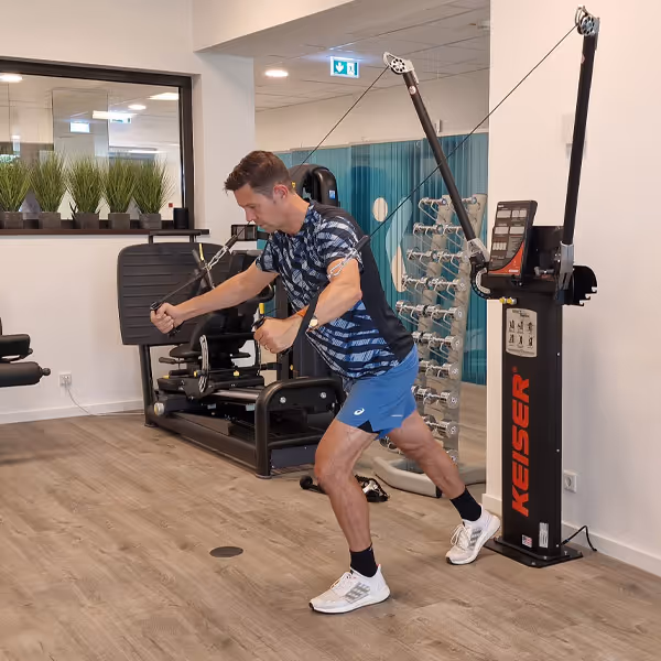 Ole Nauert, Inhaber und Therapeut der Rheinblick Physio, zeigt im Trainingsraum eine Chest Front Flys Übung am Kaiser Kabelzug.