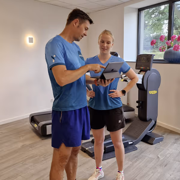 Ole Nauert, Inhaber und Therapeut der Rheinblick Physio, steht mit der Physiotherapeutin im Trainingsraum und bespricht mit ihr einen Therapieplan am IPad.