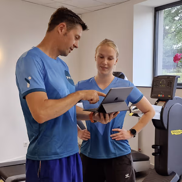Ole Nauert, Inhaber und Therapeut der Rheinblick Physio, steht mit der Physiotherapeutin im Trainingsraum und bespricht mit ihr einen Therapieplan am IPad.