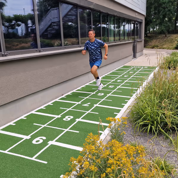 Ole Nauert, Inhaber und Therapeut der Rheinblick Physio, läuft im Außenbereich der Rheinblick Physio auf einem grünen Sprinter-Teppich.