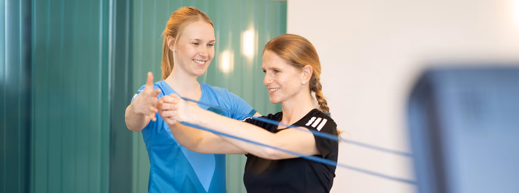 Physiotherapeutin der Rheinblick Physio trainiert mit Patientin, die eine Rückenübung mit dem Theraband durchführt.