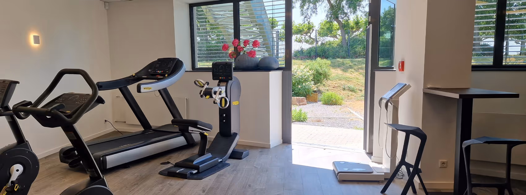 Teil des Trainingsbereichs mit Blick durch eine offene Glastür und Fenster ins Grüne nach draußen.