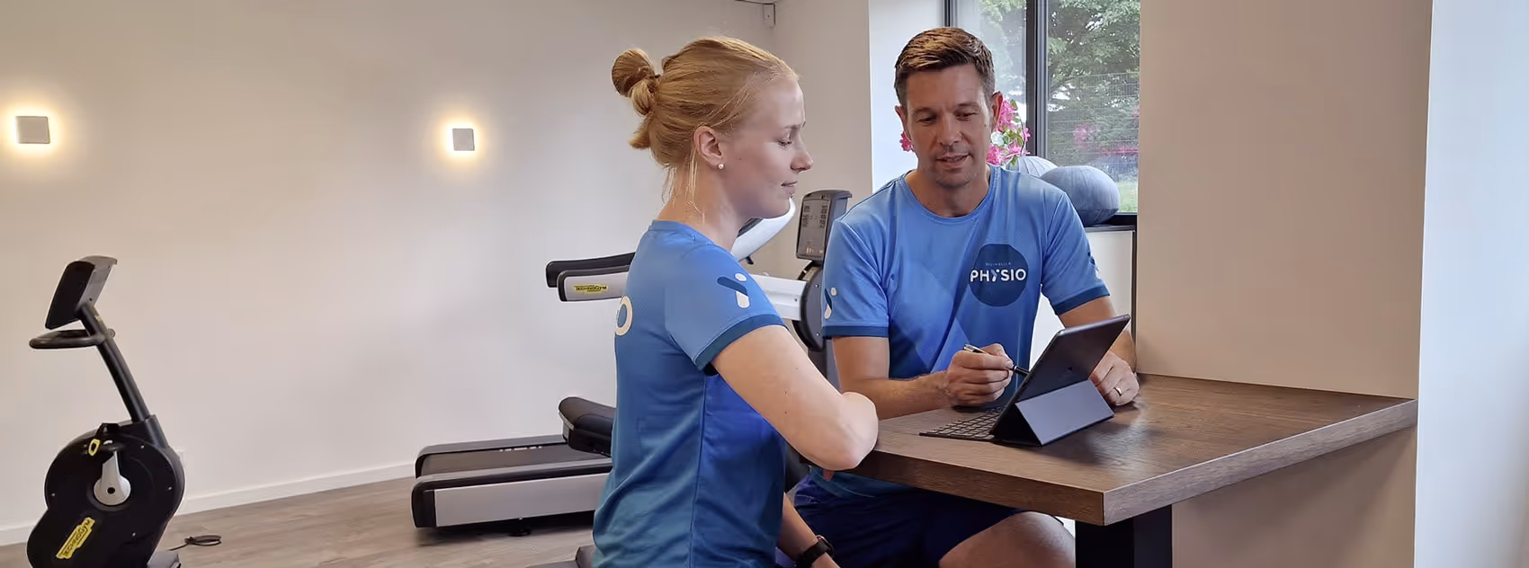 Ole Nauert, Inhaber und Therapeut der Rheinblick Physio, sitzt im Gespräch mit der Physiotherapeutin zusammen und bespricht einen Therapieplan am IPad.
