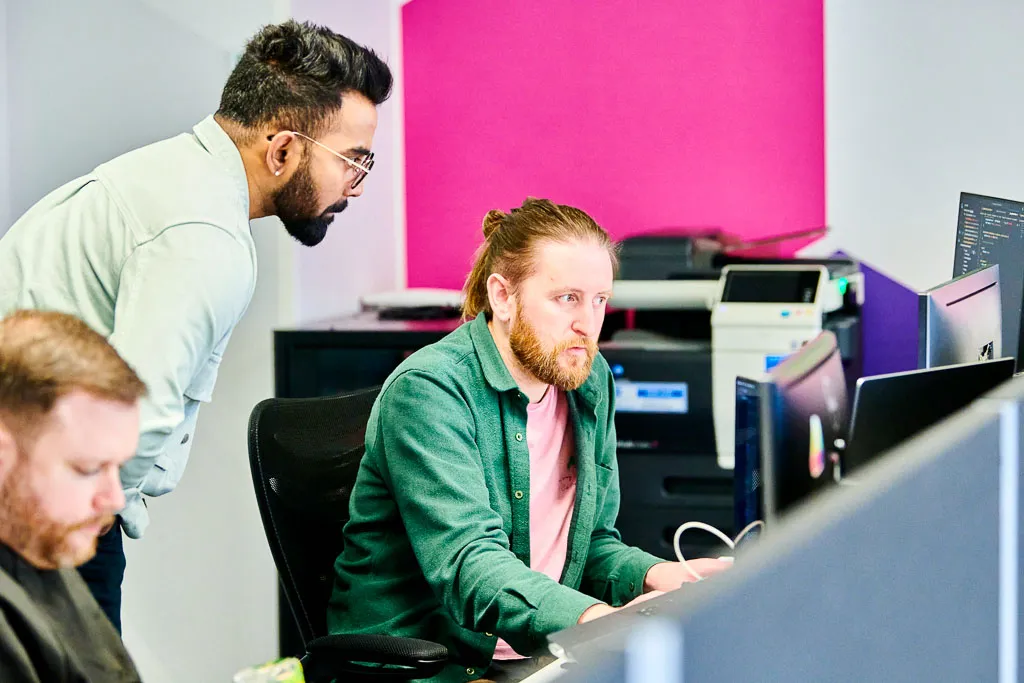 Software engineers engaged in discussion at their workspace, collaborating to resolve an issue.