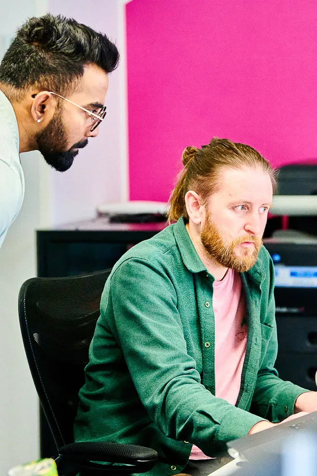 Software engineers engaged in discussion at their workspace, collaborating to resolve an issue.
