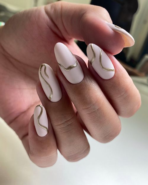 Hand with pale pink matte nails featuring thin gold wavy line nail art on each finger.