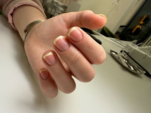 Close-up of a hand with a natural French manicure featuring nude nails and white tips.