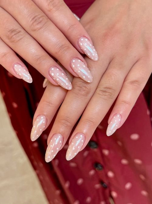 Hands with almond-shaped nails, nude polish with white polka dots, on a red polka dot dress.