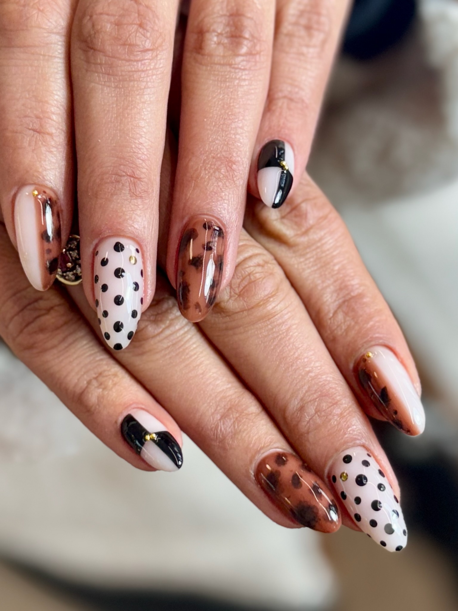 Hands with almond-shaped nails featuring black polka dots, tortoiseshell pattern, and black-and-white designs.
