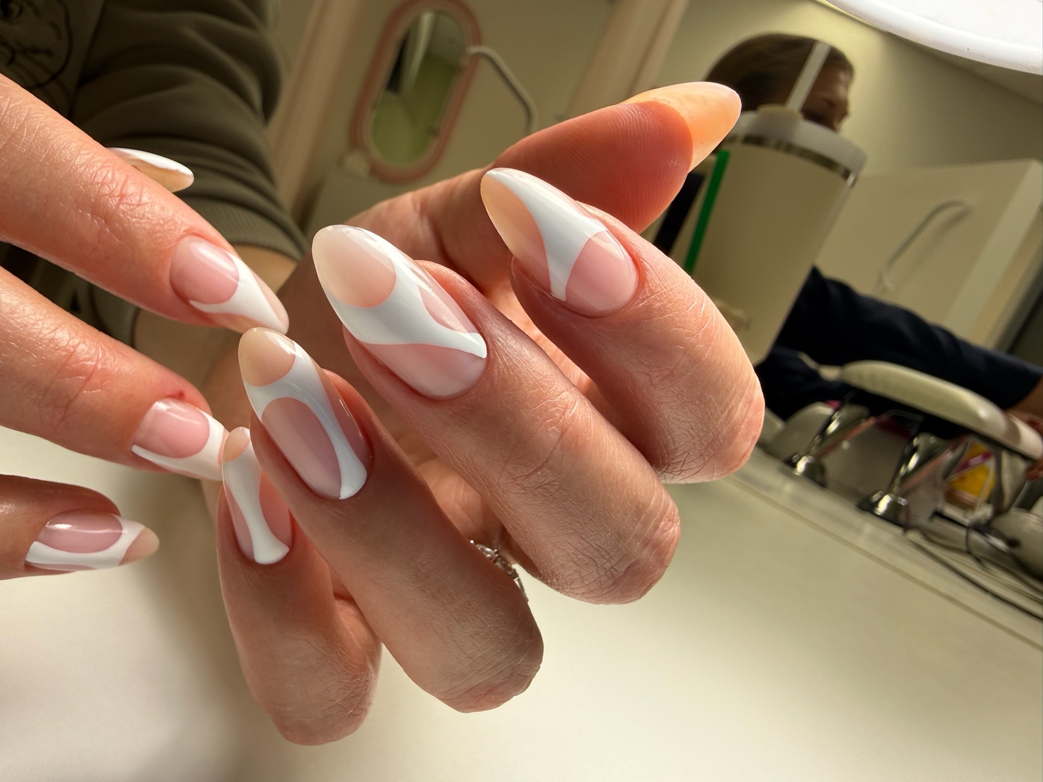 Close-up of hands with nude and white modern abstract swirl nail art on almond-shaped nails.