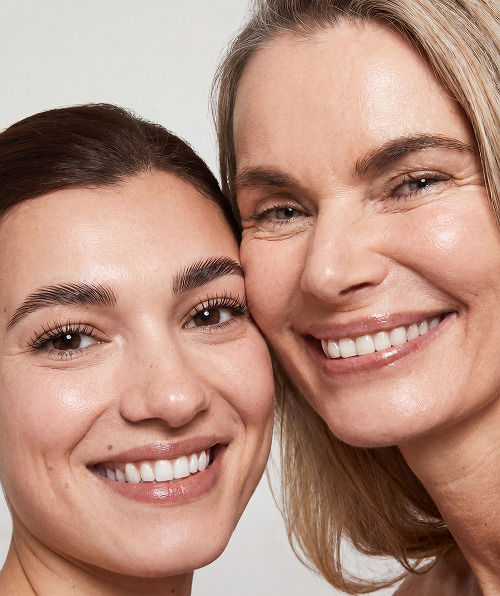 Close-up of two smiling women with clear skin, one younger with dark hair and one older with blonde hair.