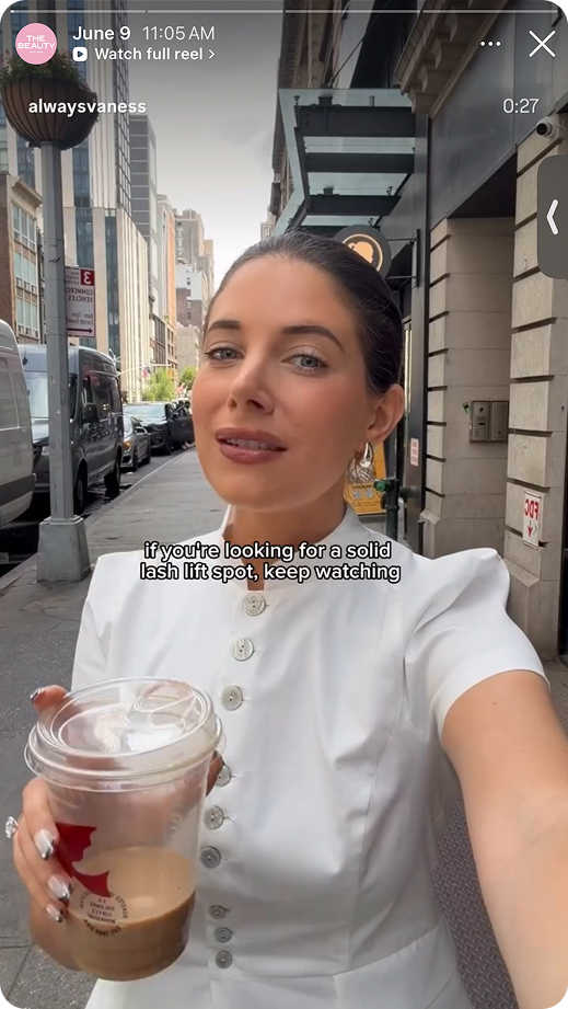 Woman in white blouse holding iced coffee cup on city street with text about lash lift spot.