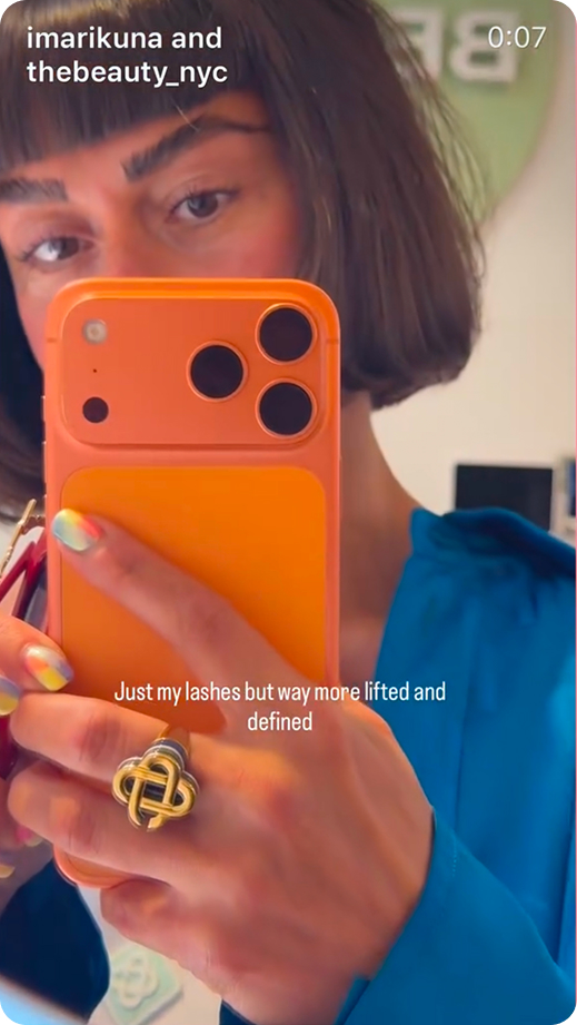 Person with dark bob haircut taking a selfie with an orange phone showing lifted, defined lashes.