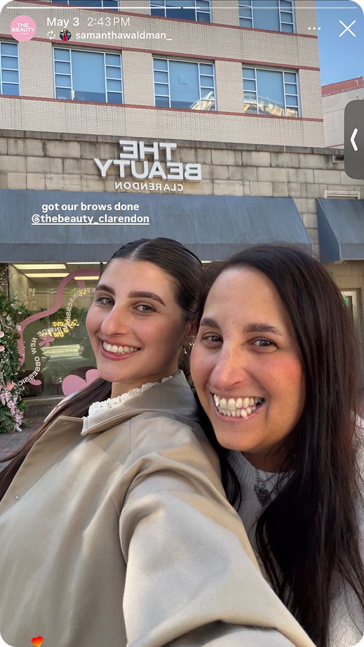 Two smiling women taking selfie outside The Beauty Clarendon salon on a sunny day.