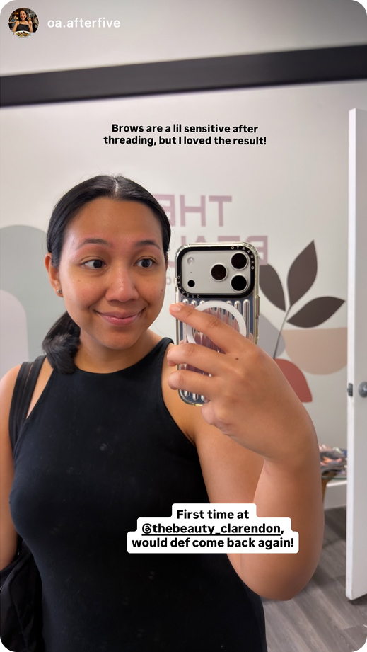 Smiling woman with freshly threaded eyebrows taking a mirror selfie in a beauty salon.