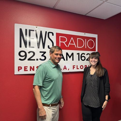 A man in green and a women in black posing in front of the News Radio 92.3 logo.