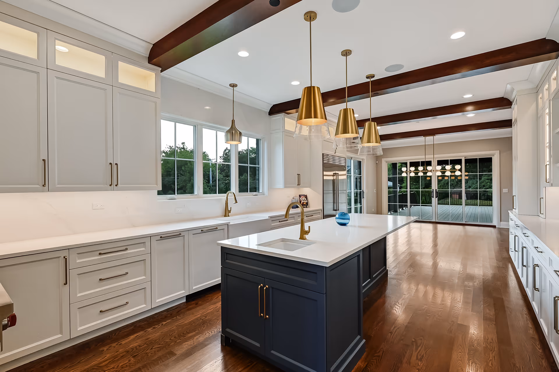 Spacious modern kitchen with white cabinets, dark blue island, gold faucets, pendant lights, and hardwood floors.