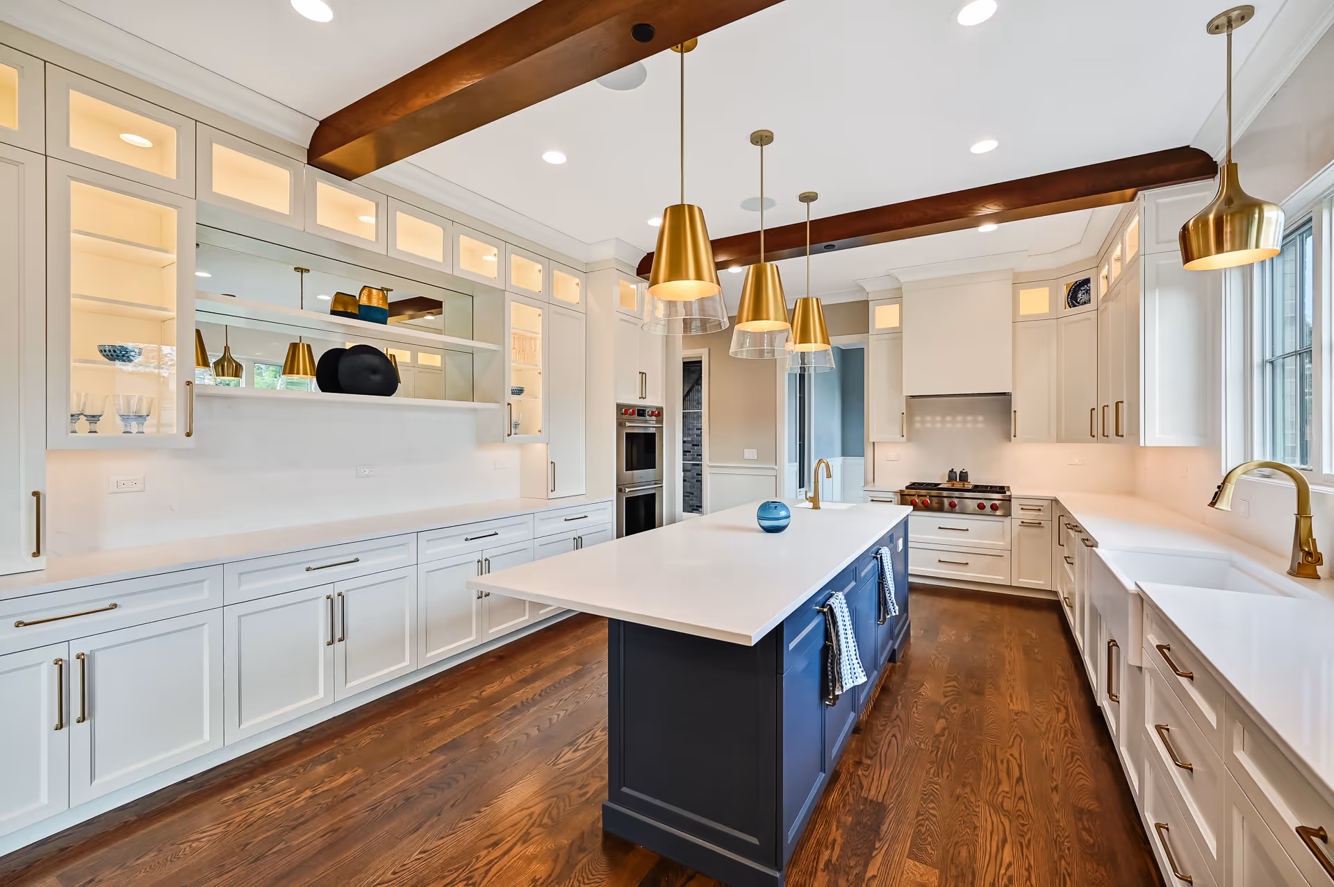 Spacious modern kitchen with white cabinetry, dark blue island, gold fixtures, hardwood floors, and pendant lights.