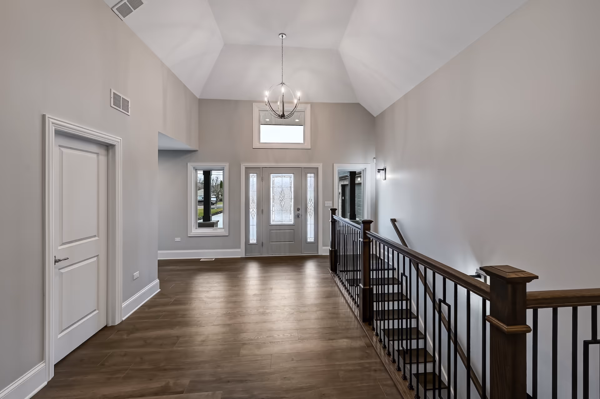 Entrance foyer with gray walls, wooden floor, decorative glass front door, and dark wood staircase railing.