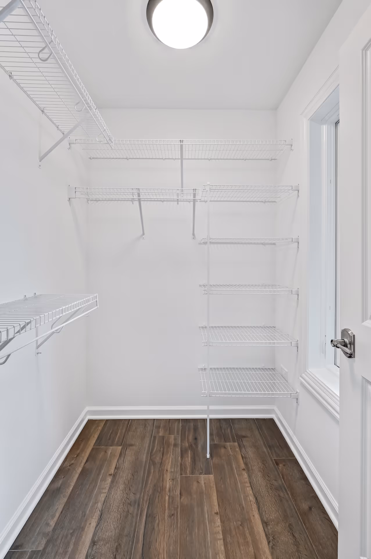 Empty walk-in closet with white wire shelves and dark wood-look flooring.