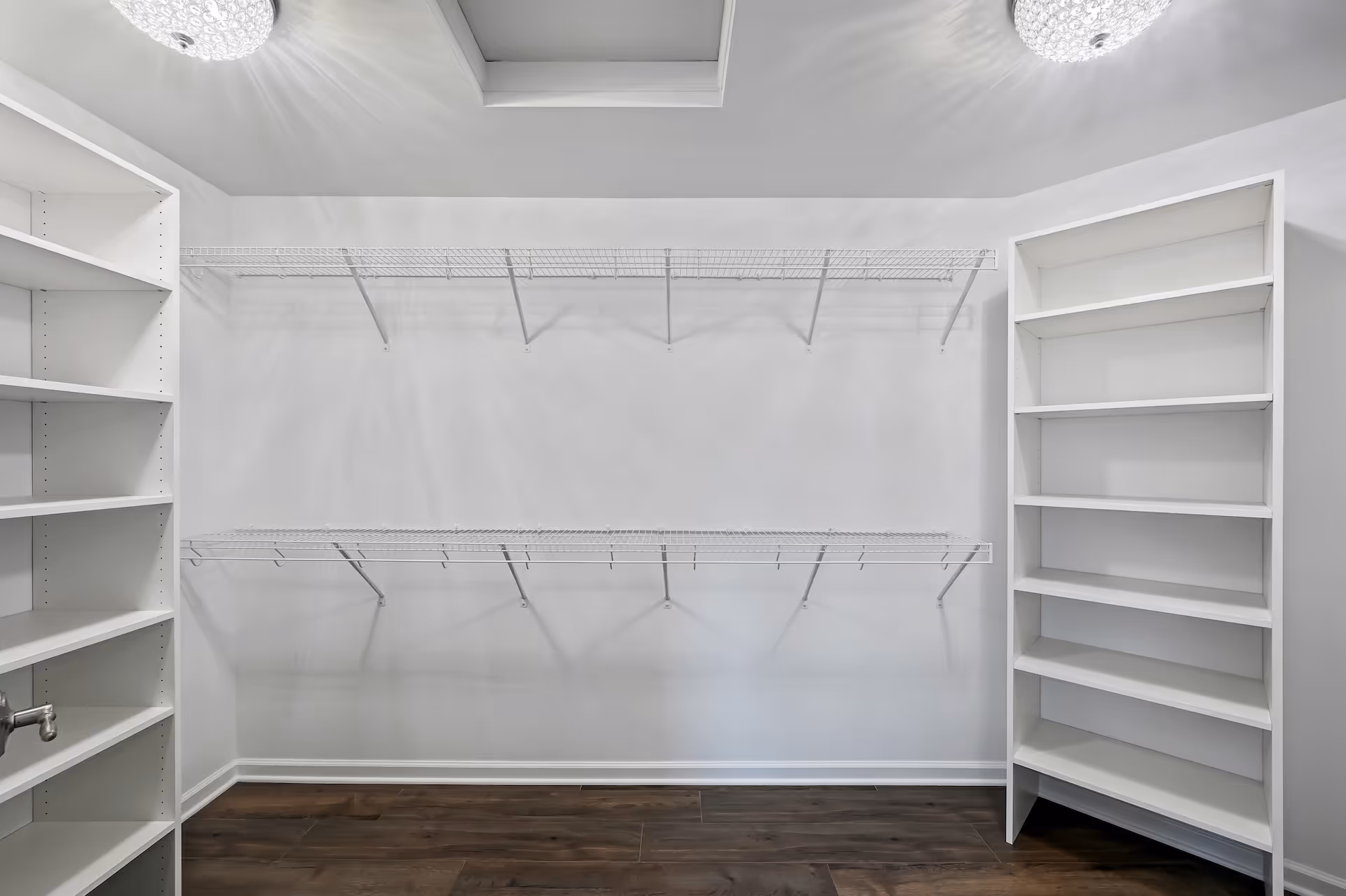 Empty walk-in closet with white shelves on both sides, two wire racks on the back wall, and dark wooden floor.