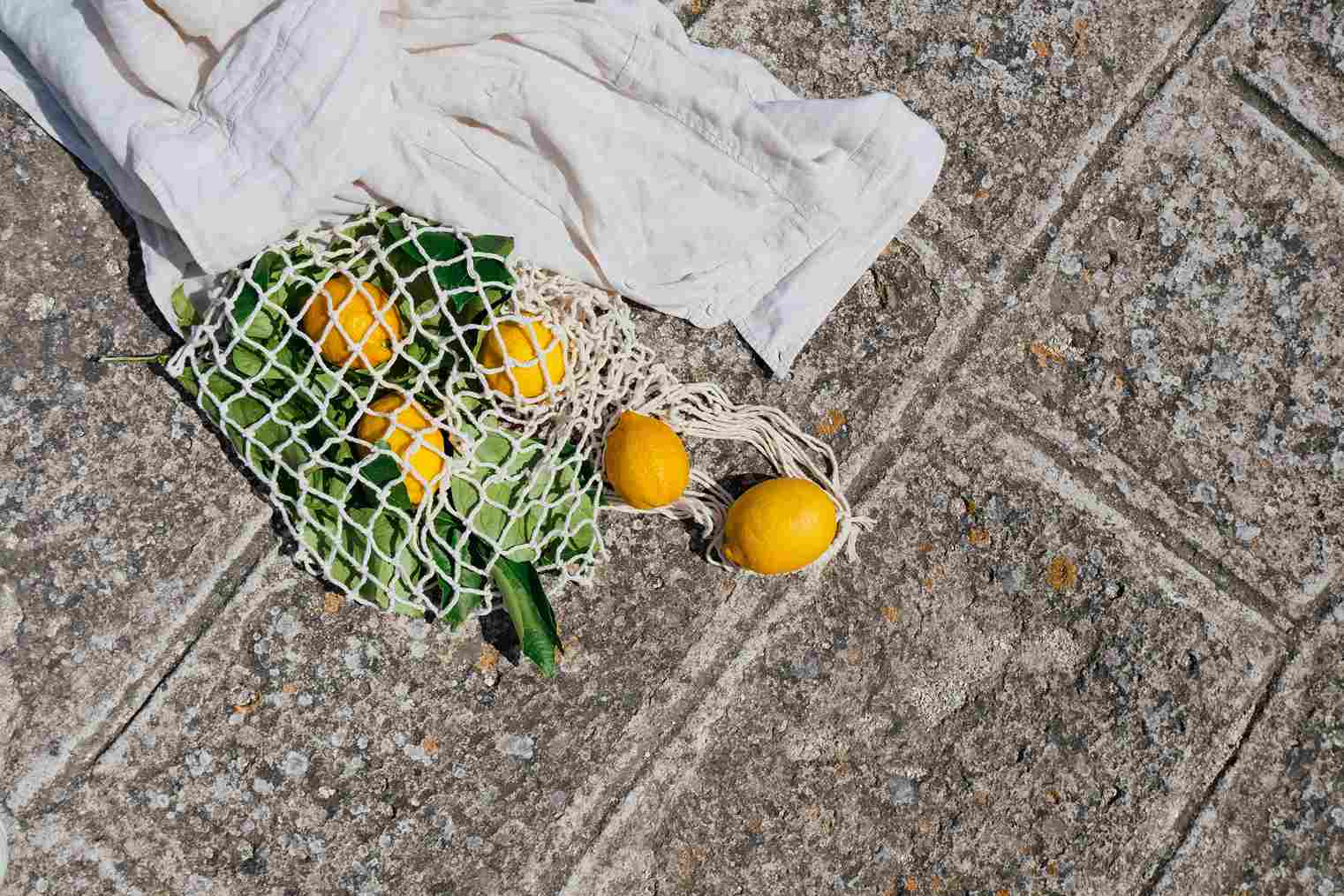 a reusable bag full of lemons next to a linen coverup