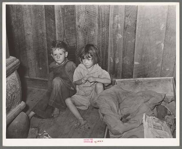 Two thin and bedraggled children sitting on a rough floor