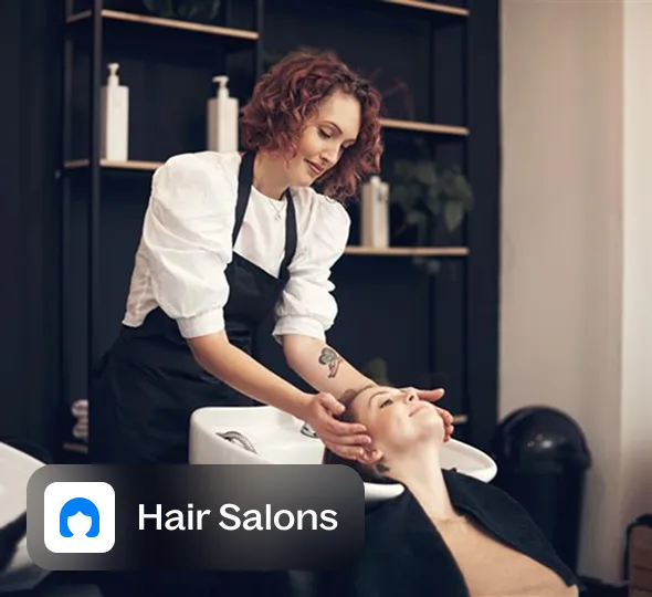 Hairdresser washing a client's hair at a salon sink.
