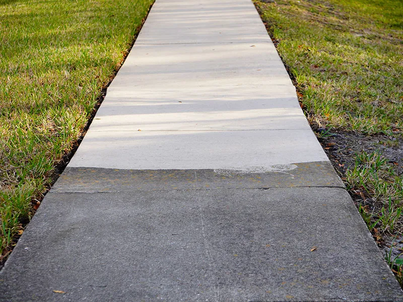 a sidewalk leading to a grassy area with trees in the background