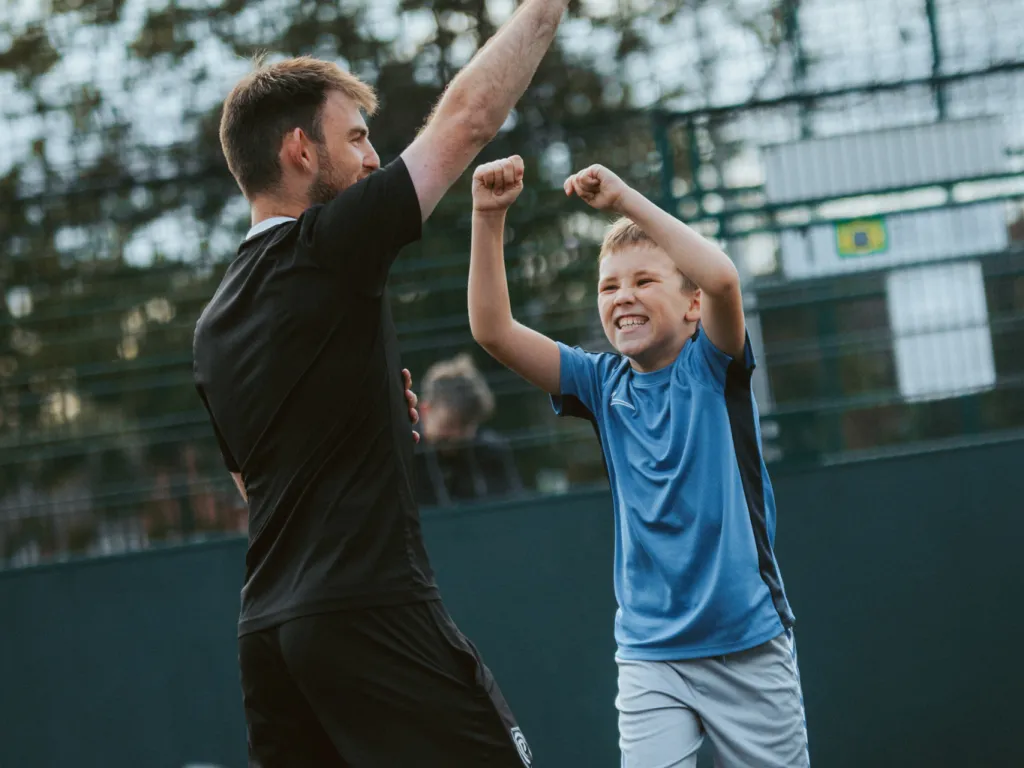 Man and young boy celebrating outdoors with raised arms and smiles during a sports activity.
