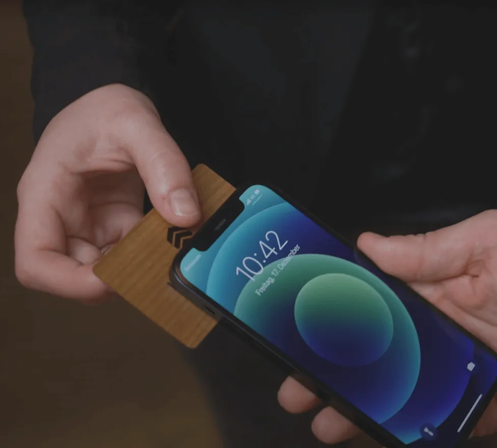 Person holding a smartphone with a blue and green abstract wallpaper while another hand inserts a brown card behind it.
