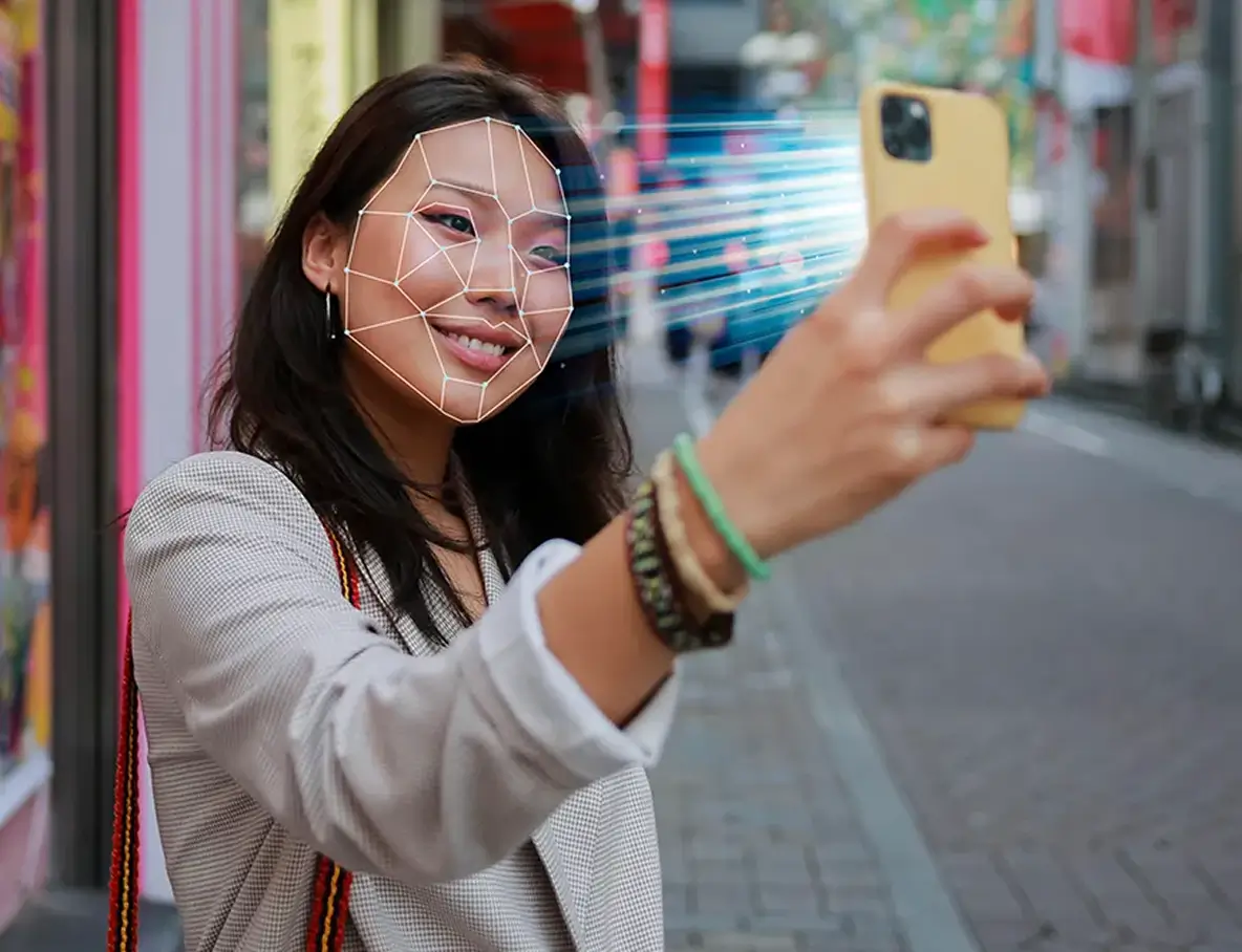 Woman smiling for a smartphone selfie with facial recognition patterns and light beams scanning her face.