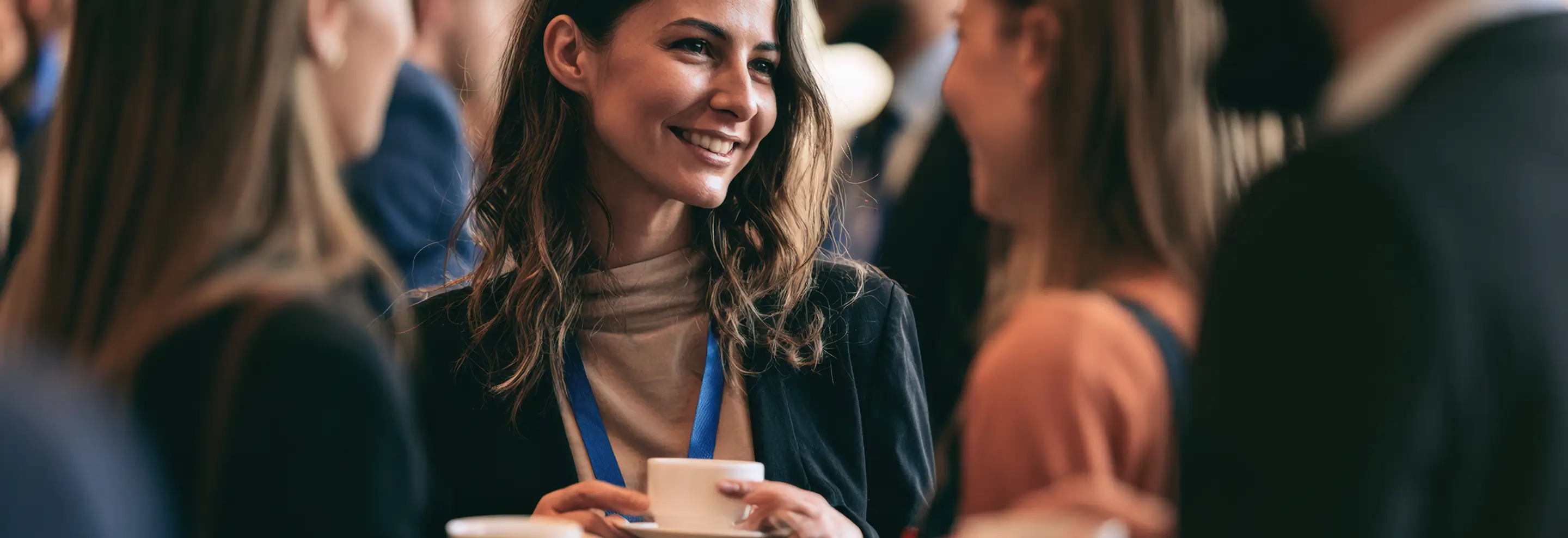 Smiling woman holding a coffee cup in a lively networking event or social gathering.