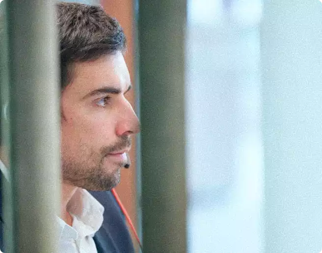 Ein Mann mit Headset, der nach rechts blickt, vor einem verschwommenen hellblauen Hintergrund.