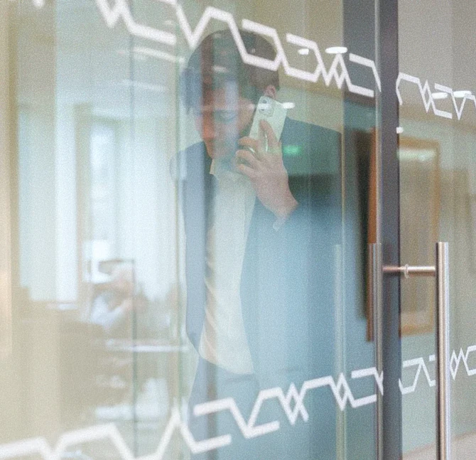 Homme d'affaires parlant au téléphone dans un bureau à travers une porte vitrée avec motifs blancs.