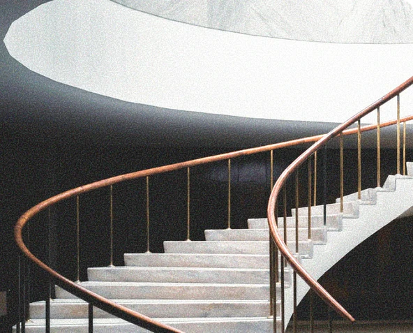 Escalier en colimaçon en béton avec rampe en bois et barres métalliques dorées dans un environnement moderne.