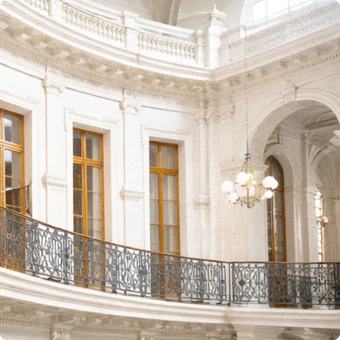 Eine schmiedeeiserne Balustrade mit großen Fenstern mit Holzrahmen und einem hängenden Kronleuchter in einem klassisch gestalteten Innenraum.