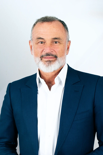 Uomo maturo con la barba grigia, che indossa una camicia bianca e un blazer blu, mentre guarda verso la fotocamera.