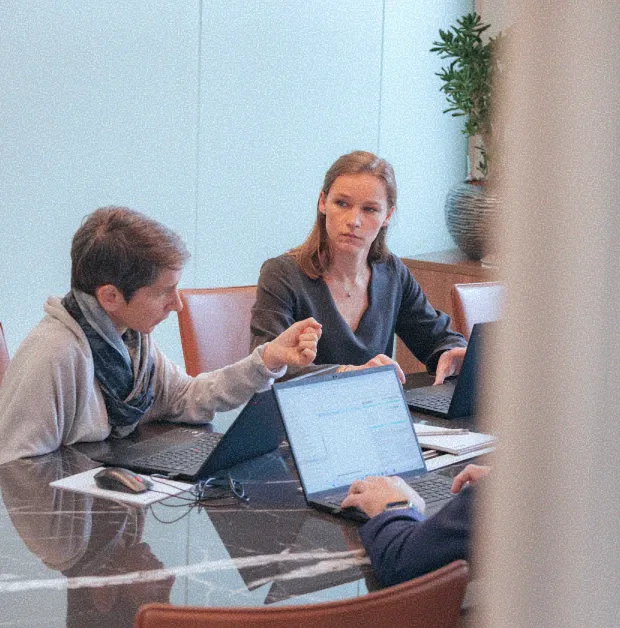 Zwei Frauen, die an einem Marmortisch in einem Besprechungsraum ernsthaft vor ihren Laptops diskutieren.