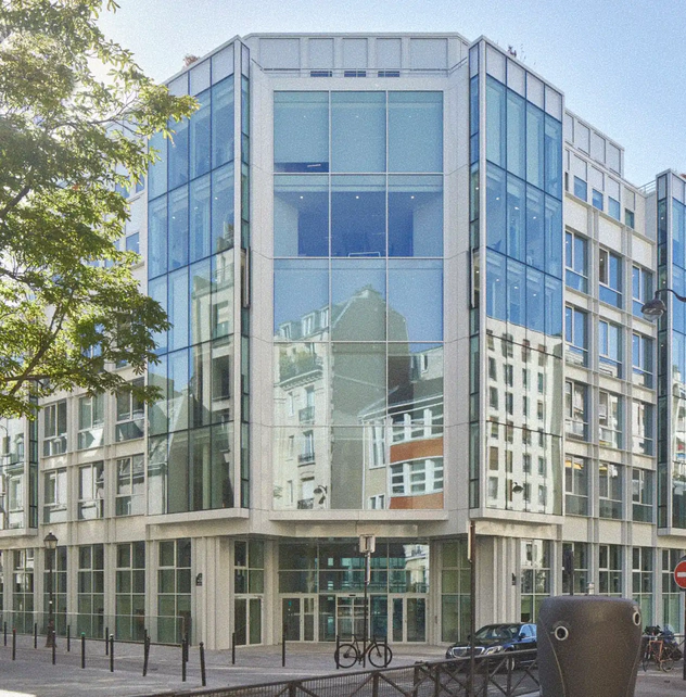 Moderno edificio in vetro e cemento che richiama lo stile degli edifici antichi, con un ingresso principale e una bicicletta parcheggiata davanti.