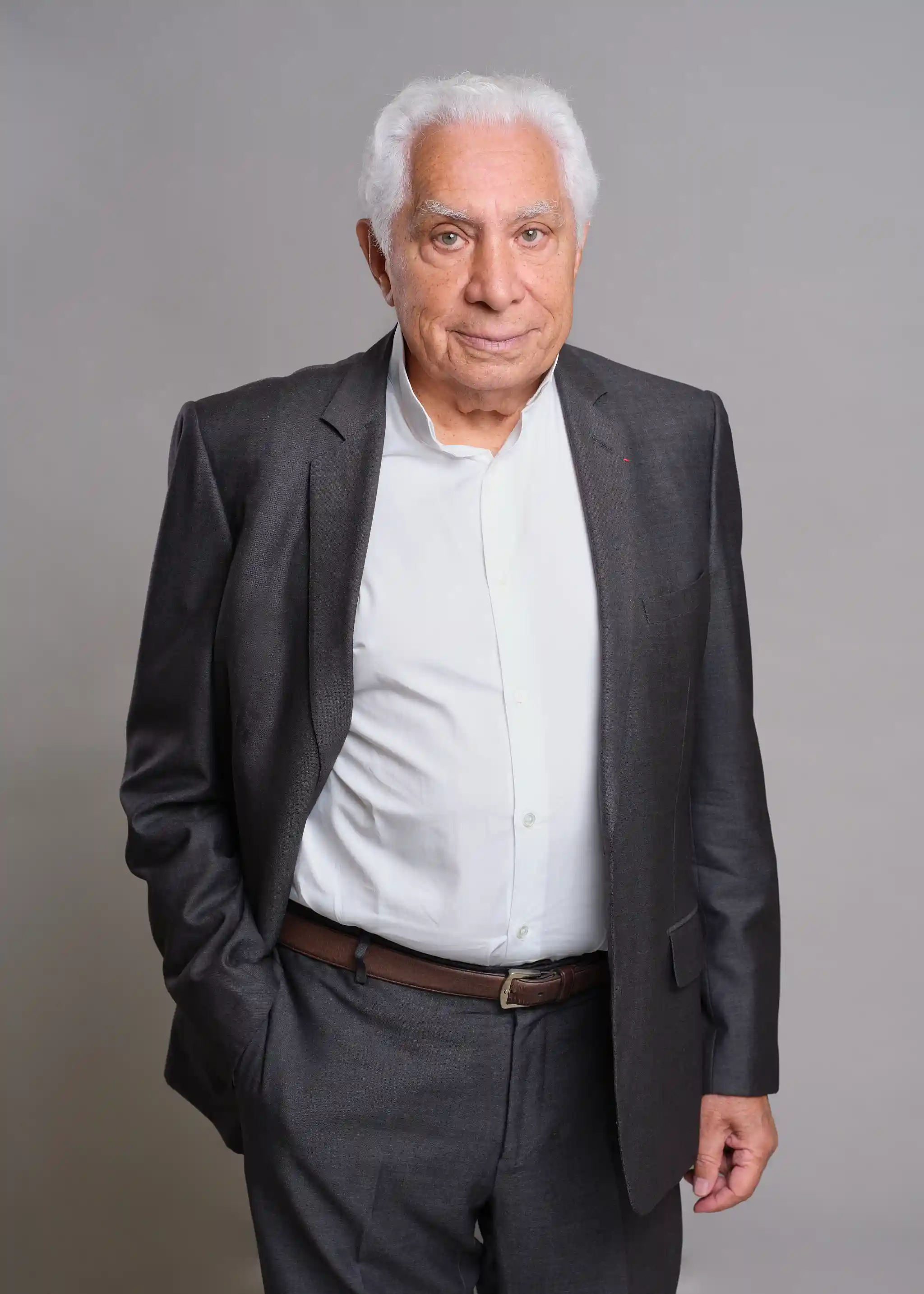 Portrait of an elderly man with white hair, wearing a light-colored shirt and a navy blue suit with thin stripes.