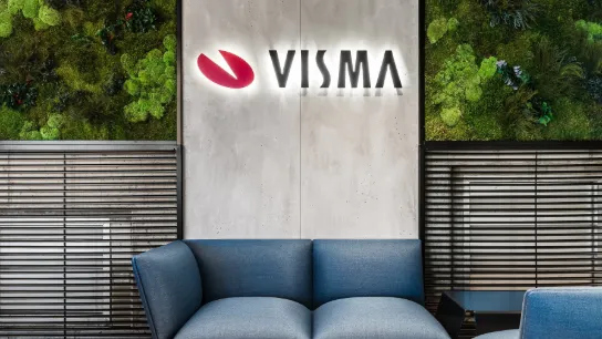 Logo lumineux de Visma sur un mur d’accueil moderne avec canapé bleu et mur végétal