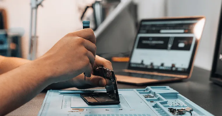 Main réparant un boîtier à l'aide d'un tournevis, PC portable en arrière-plan