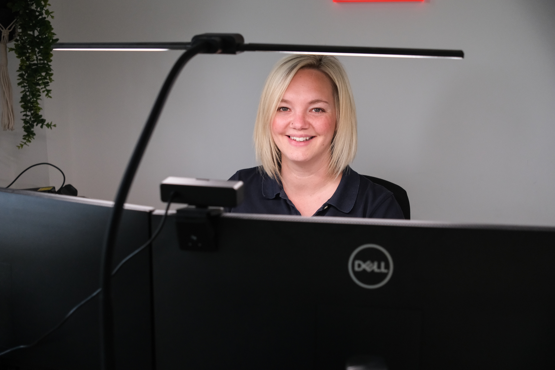 Smiling woman with blonde hair sitting behind a Dell computer monitor in an office.